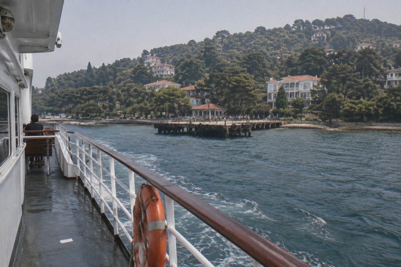 White ferry approaching a wooden pier on a green island hillside in Istanbul
