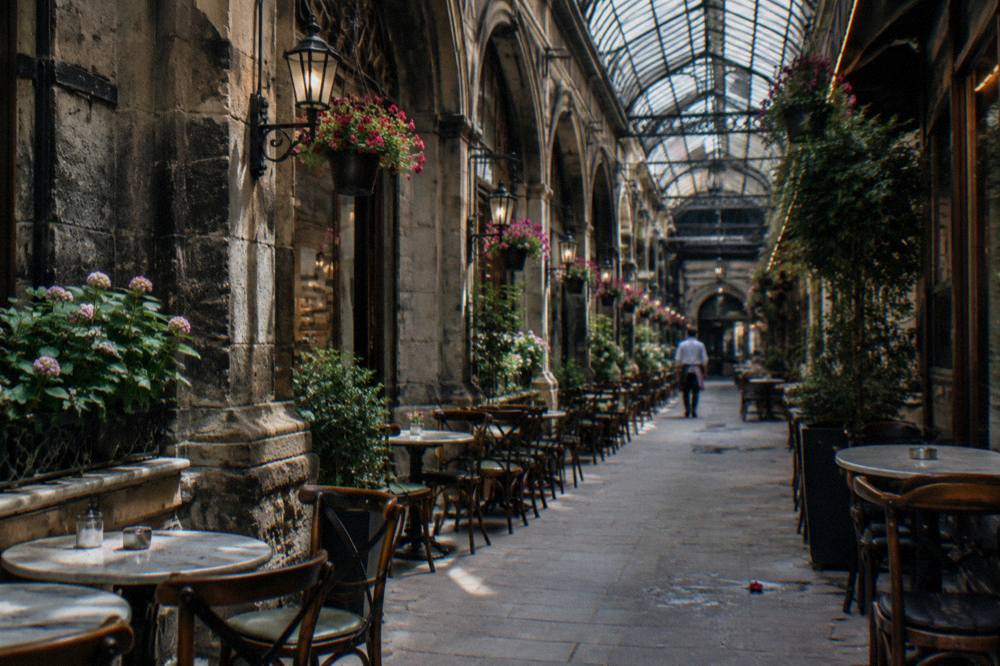 A historic covered passage with ornate ceilings and small shopfronts off a busy pedestrian avenue