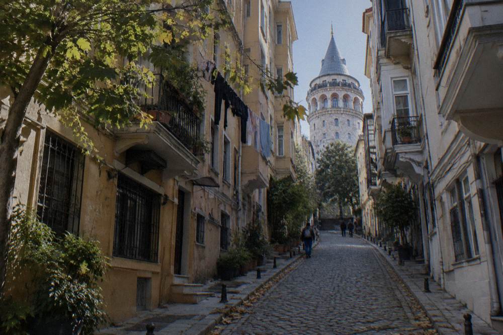 A narrow cobbled lane with old apartment buildings climbing a hill toward a stone tower