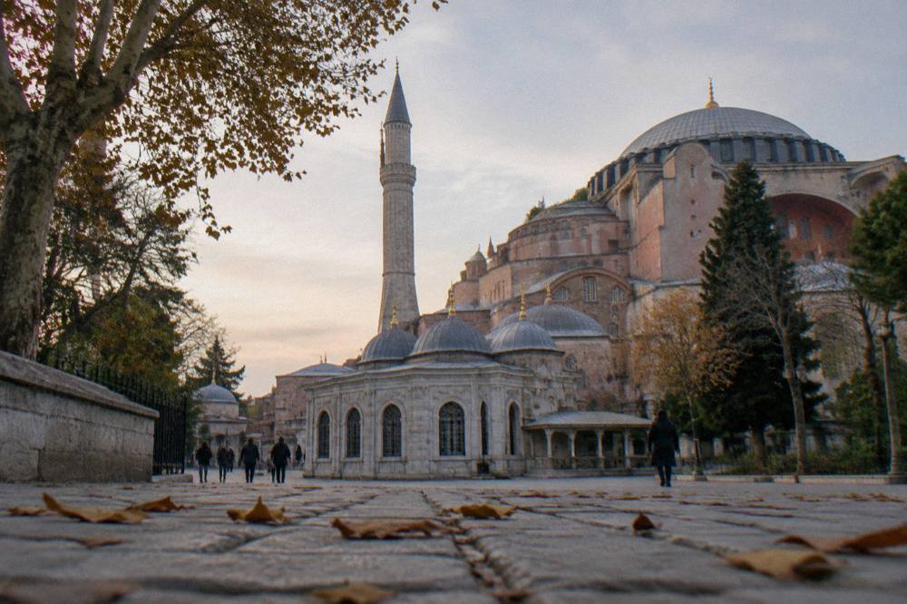 Stone courtyard of an Ottoman mosque with small domes and a minaret against the sky
