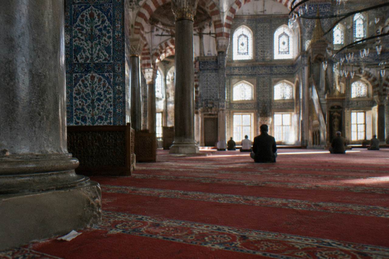 Ornate tiled interior arcade of a historic Istanbul mosque with patterned carpet and filtered daylight