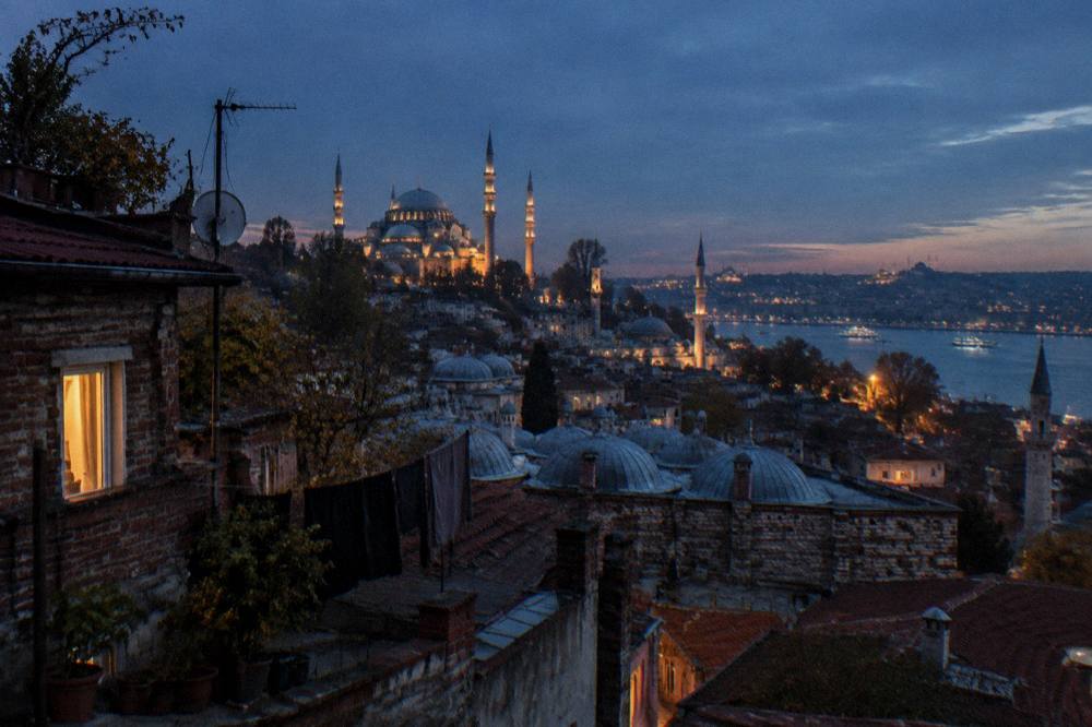 Wide evening view of Istanbul's old city skyline with illuminated domes and minarets from a rooftop terrace