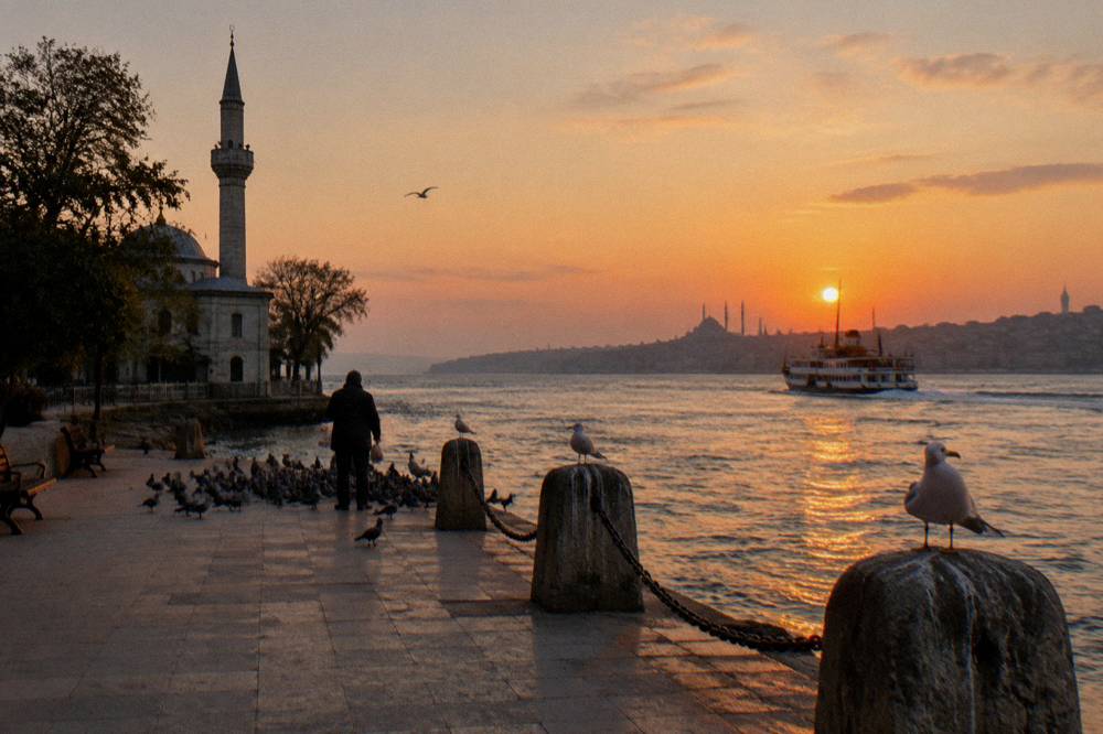 Waterfront square with a mosque silhouette and calm water at golden hour