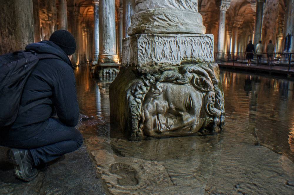 A carved Medusa head serving as the base of a stone column in low light