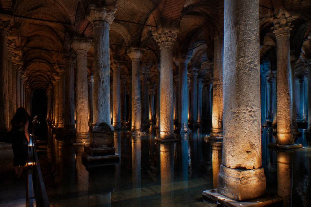 A long row of illuminated columns receding into darkness above still water
