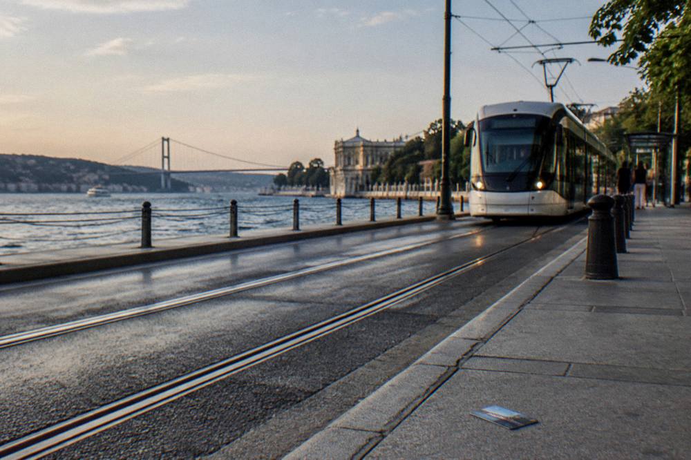 Modern tram travelling along a waterside street with the shoreline behind