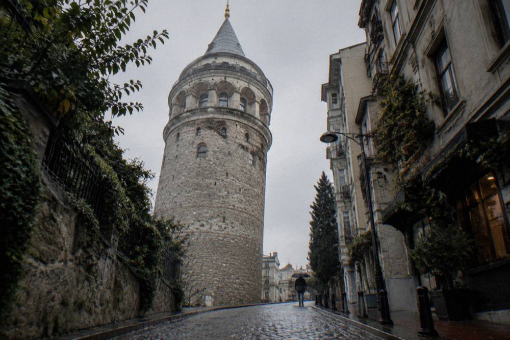 Medieval stone walls of Galata Tower seen from a narrow sloping street below